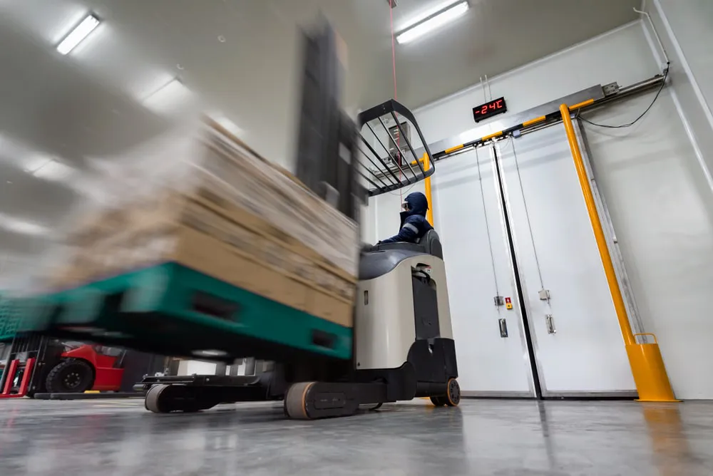 Forklift operator moving pallets in modern warehouse cold storage facility