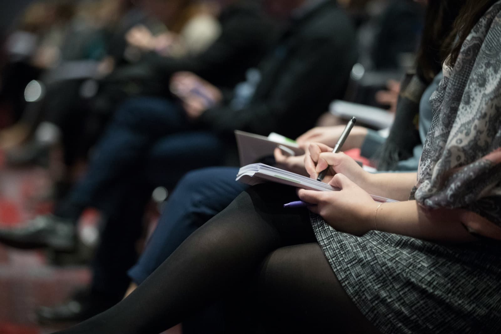 Conference audience seated and taking notes during a presentation