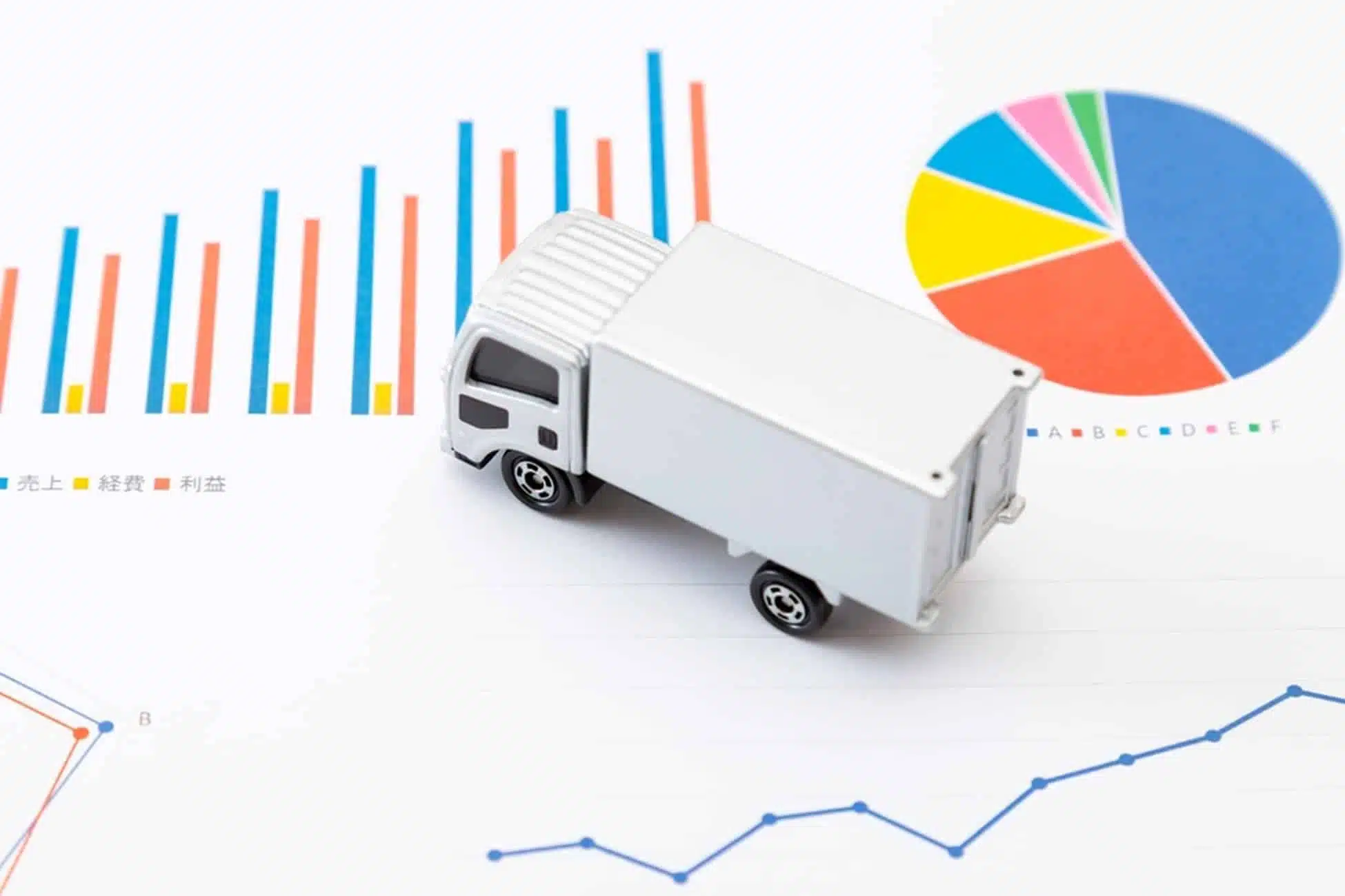 White toy truck surrounded by colorful business charts and graphs showing freight management data