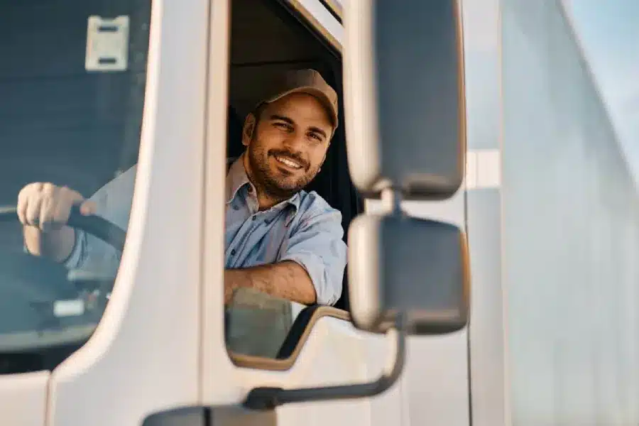 Smiling truck driver in baseball cap looking out of white truck cab window