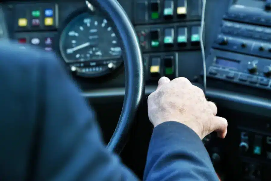 Driver's hand on steering wheel inside semi truck cabin with dashboard gauges