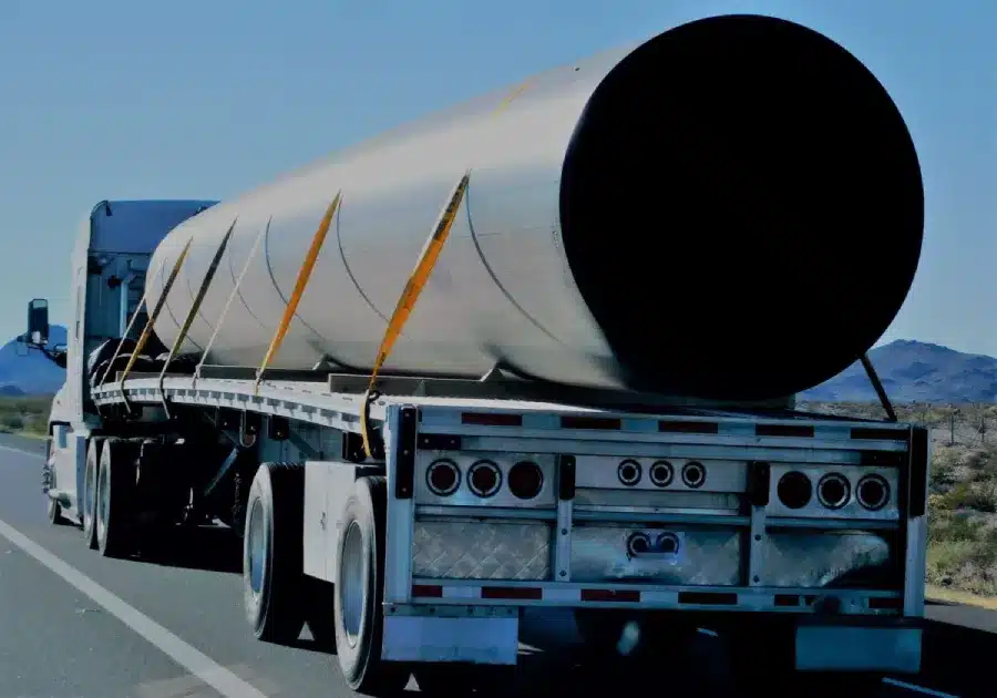 Semi-truck hauling large white cylindrical cargo on desert highway