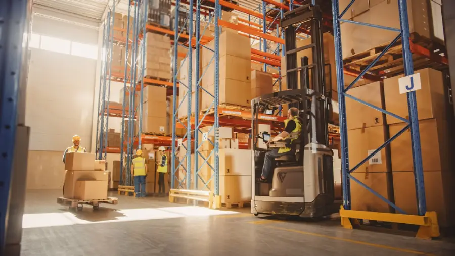 Forklift operator moving boxes in modern warehouse with tall storage racks