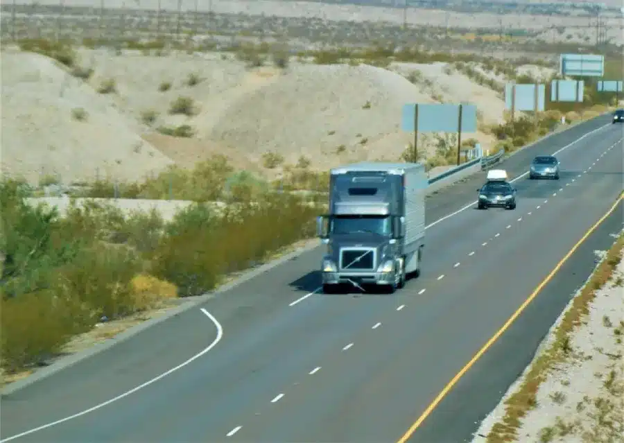 Semi-truck driving on desert highway with cars in arid landscape