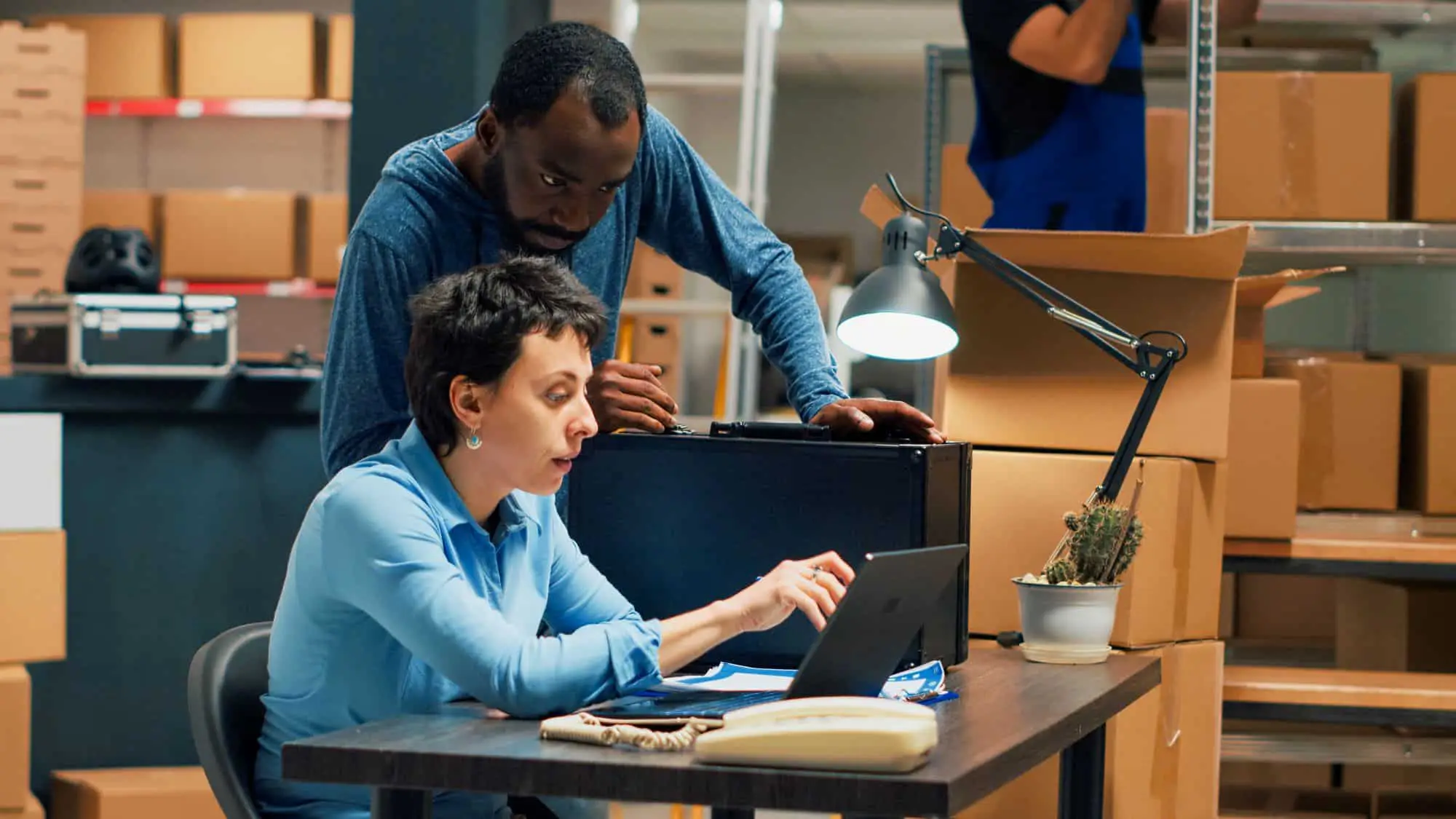 Two warehouse employees collaborating on laptop to plan storage and shipment logistics