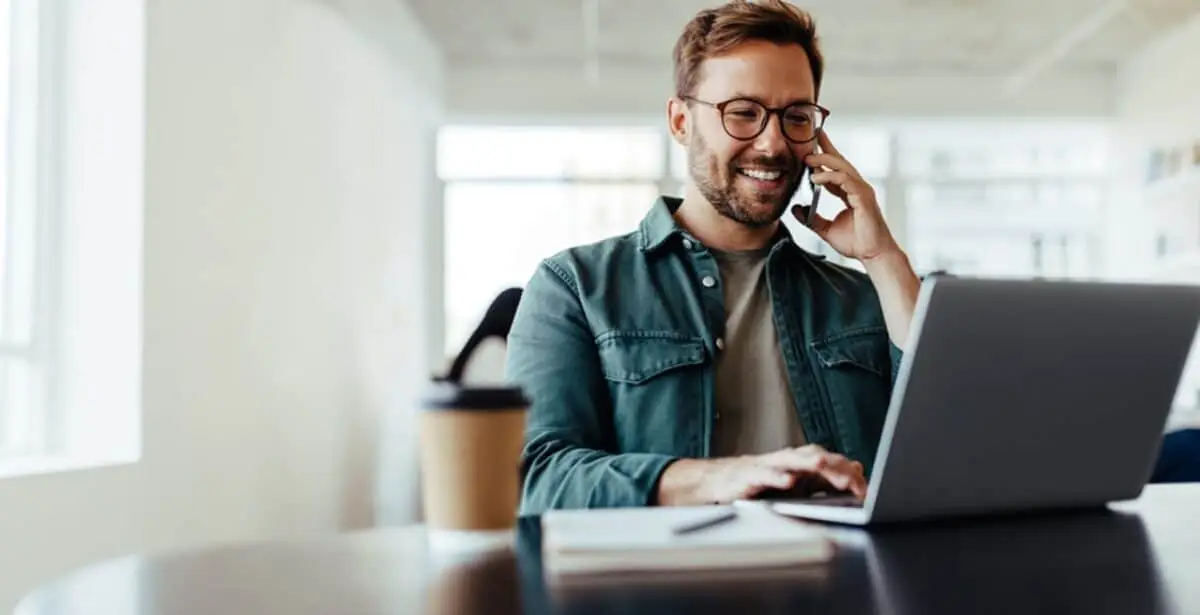 Professional businessman talking on phone while working on laptop in modern office