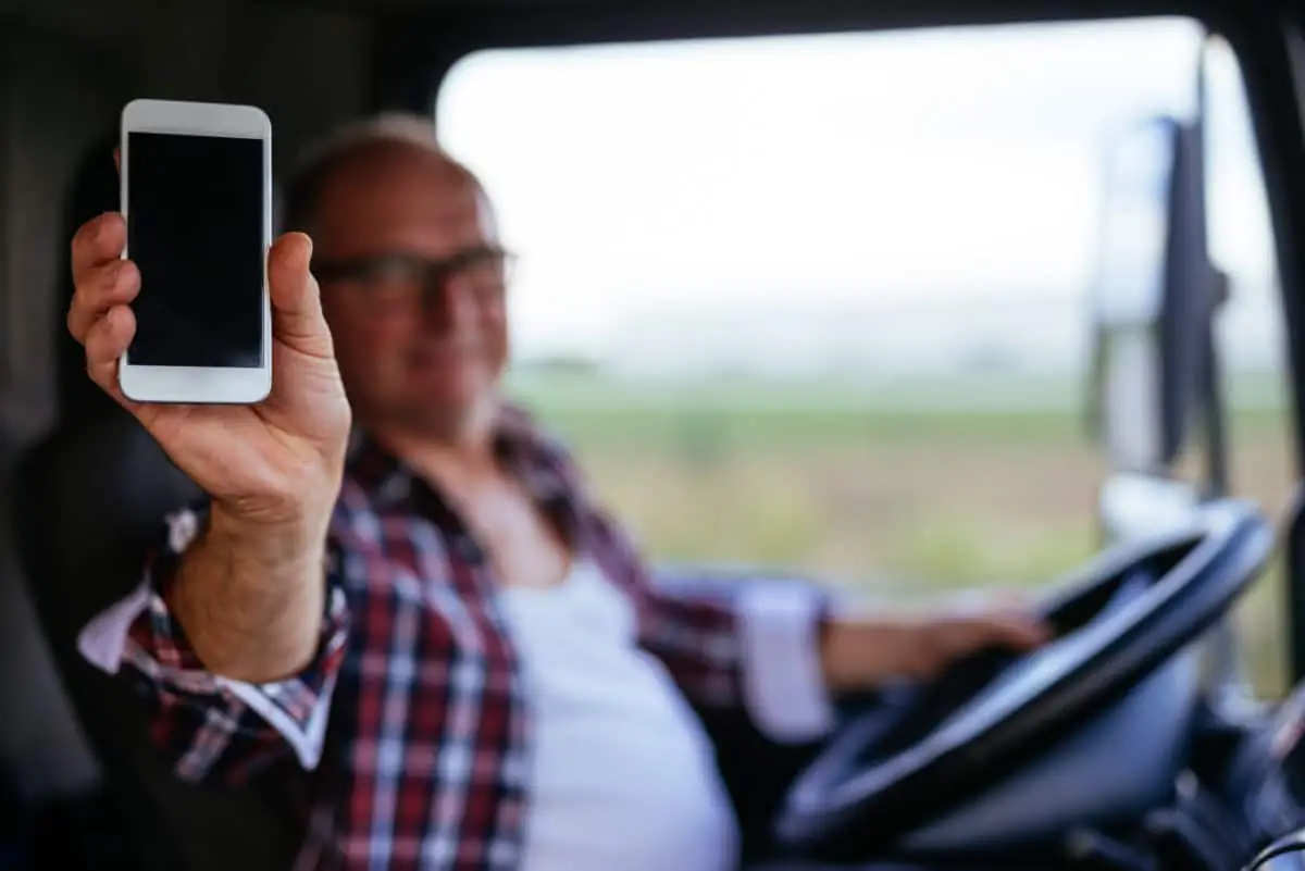 Man in plaid shirt holding smartphone while driving vehicle, showing distracted driving behavior