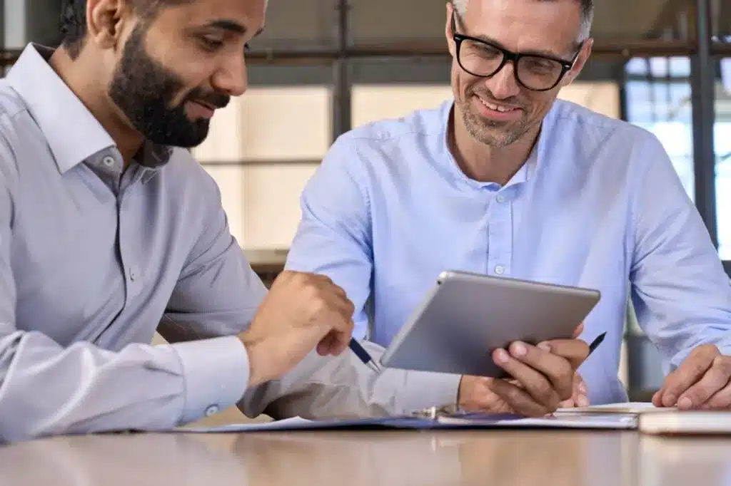 Two businessmen analyzing data and reports on tablet in modern office