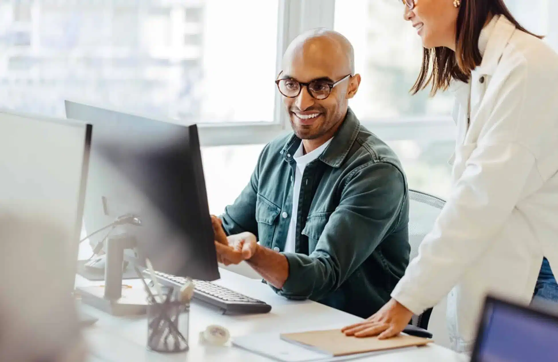 Two professional colleagues collaborating at desktop computer in modern office workspace