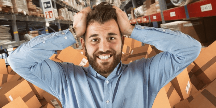 man with hands on his head with a pile of boxes in a warehouse in the background