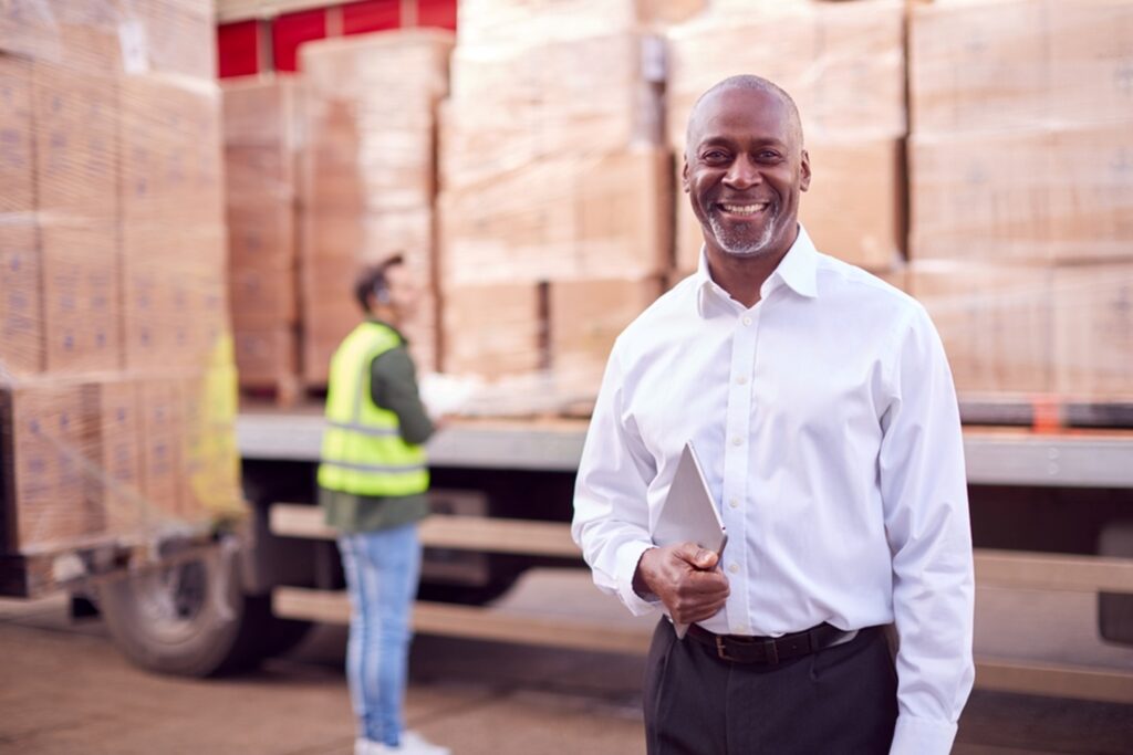 business man holding a tablet in fornt of a semi truck loaded with pallets full of boxes