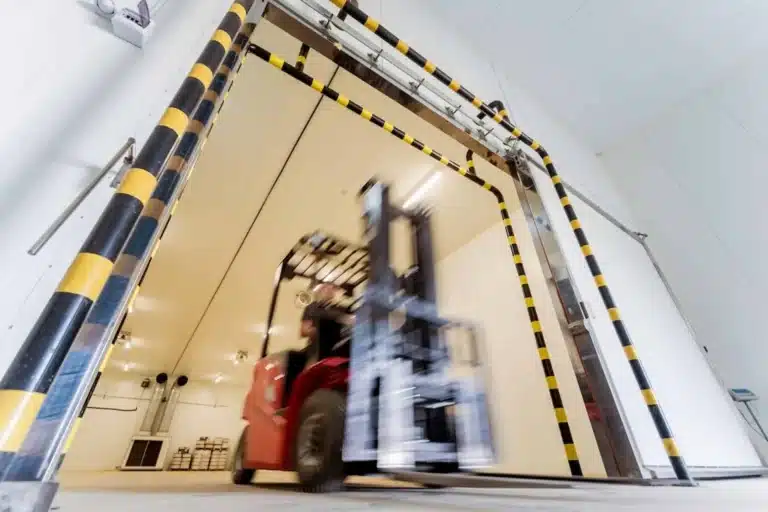 Workers exiting insulated cold storage doors with yellow safety striping in warehouse facility