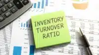 Inventory turnover ratio written on green sticky note with financial documents and charts