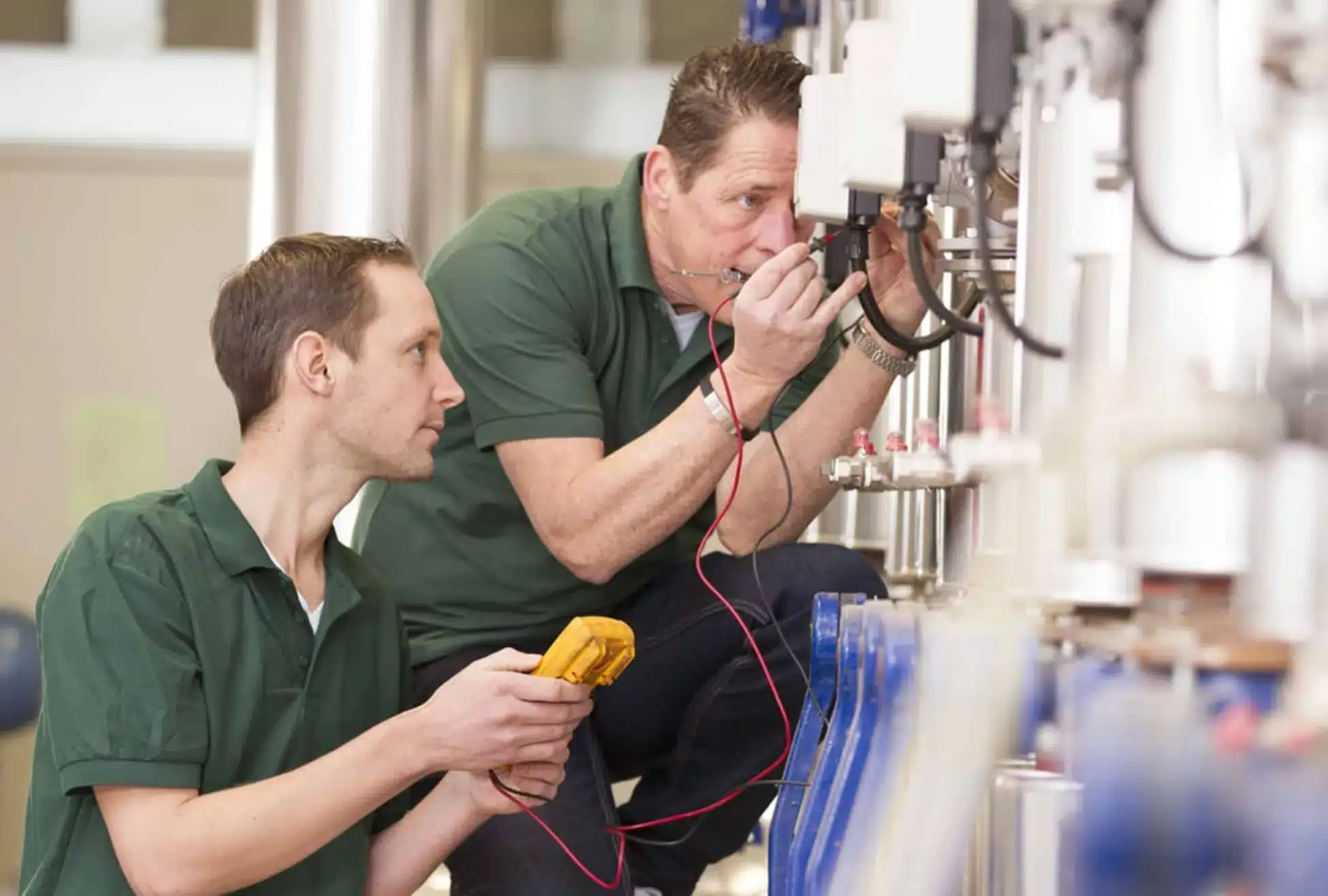 Two technicians performing maintenance inspection on industrial equipment with testing tools